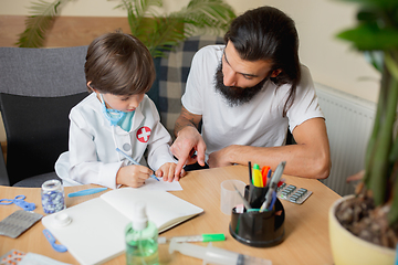 Image showing Little boy playing pretends like doctor examining a man in comfortabe medical office