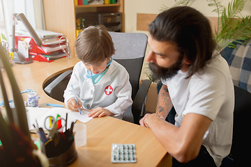 Image showing Little boy playing pretends like doctor examining a man in comfortabe medical office