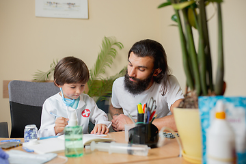 Image showing Little boy playing pretends like doctor examining a man in comfortabe medical office