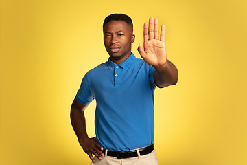 Image showing Young african-american man\'s portrait isolated on yellow studio background, facial expression. Beautiful male half-lenght portrait with copyspace.