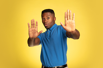 Image showing Young african-american man\'s portrait isolated on yellow studio background, facial expression. Beautiful male half-lenght portrait with copyspace.