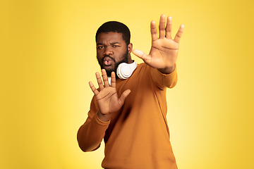 Image showing Young african-american man\'s portrait isolated on yellow studio background, facial expression. Beautiful male half-lenght portrait with copyspace.