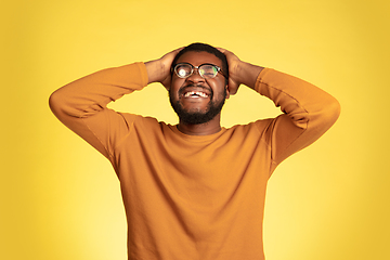 Image showing Young african-american man\'s portrait isolated on yellow studio background, facial expression. Beautiful male half-lenght portrait with copyspace.