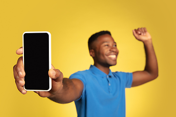 Image showing Young african-american man\'s portrait isolated on yellow studio background, facial expression. Beautiful male half-lenght portrait with copyspace.