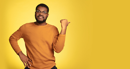 Image showing Young african-american man\'s portrait isolated on yellow studio background, facial expression. Beautiful male half-lenght portrait with copyspace.