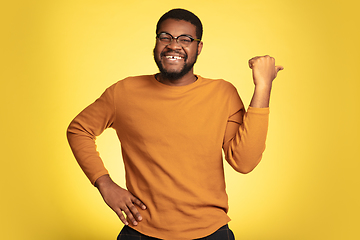 Image showing Young african-american man\'s portrait isolated on yellow studio background, facial expression. Beautiful male half-lenght portrait with copyspace.