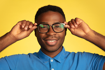 Image showing Young african-american man\'s portrait isolated on yellow studio background, facial expression. Beautiful male half-lenght portrait with copyspace.