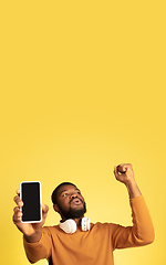 Image showing Young african-american man\'s portrait isolated on yellow studio background, facial expression. Beautiful male half-lenght portrait with copyspace.