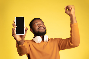 Image showing Young african-american man\'s portrait isolated on yellow studio background, facial expression. Beautiful male half-lenght portrait with copyspace.