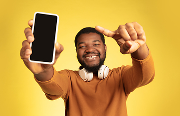 Image showing Young african-american man\'s portrait isolated on yellow studio background, facial expression. Beautiful male half-lenght portrait with copyspace.