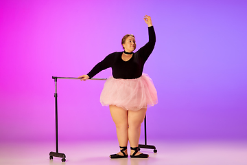 Image showing Beautiful caucasian plus size model practicing ballet dance on gradient purple-pink studio background in neon light