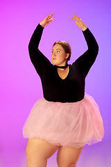 Image showing Beautiful caucasian plus size model practicing ballet dance on gradient purple-pink studio background in neon light