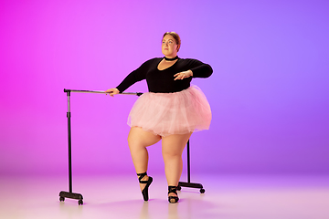 Image showing Beautiful caucasian plus size model practicing ballet dance on gradient purple-pink studio background in neon light