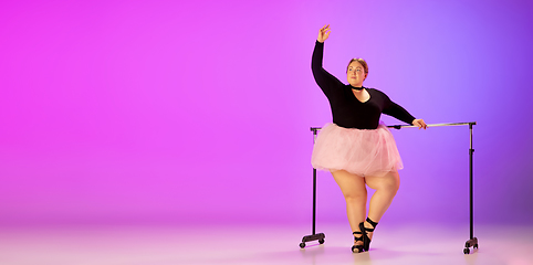 Image showing Beautiful caucasian plus size model practicing ballet dance on gradient purple-pink studio background in neon light