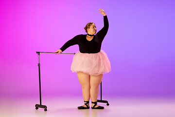 Image showing Beautiful caucasian plus size model practicing ballet dance on gradient purple-pink studio background in neon light