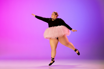 Image showing Beautiful caucasian plus size model practicing ballet dance on gradient purple-pink studio background in neon light