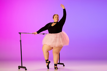 Image showing Beautiful caucasian plus size model practicing ballet dance on gradient purple-pink studio background in neon light