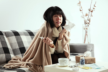 Image showing Woman wrapped in a plaid looks sick, ill, sneezing and coughing sitting at home indoors