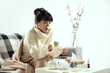 Image showing Woman wrapped in a plaid looks sick, ill, sneezing and coughing sitting at home indoors