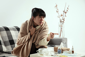 Image showing Woman wrapped in a plaid looks sick, ill, sneezing and coughing sitting at home indoors