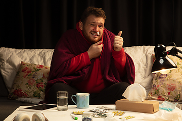 Image showing Man wrapped in a plaid looks sick, ill, sneezing and coughing sitting at home indoors