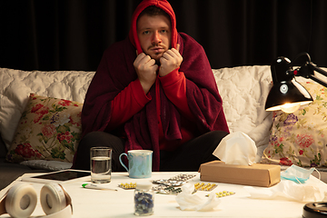 Image showing Man wrapped in a plaid looks sick, ill, sneezing and coughing sitting at home indoors