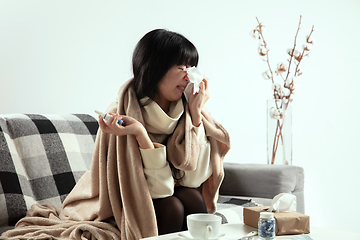 Image showing Woman wrapped in a plaid looks sick, ill, sneezing and coughing sitting at home indoors