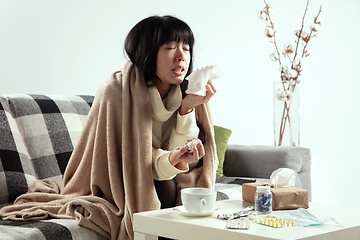 Image showing Woman wrapped in a plaid looks sick, ill, sneezing and coughing sitting at home indoors