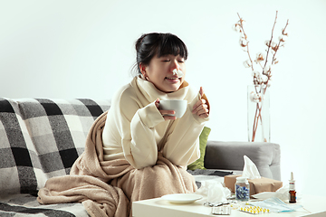 Image showing Woman wrapped in a plaid looks sick, ill, sneezing and coughing sitting at home indoors