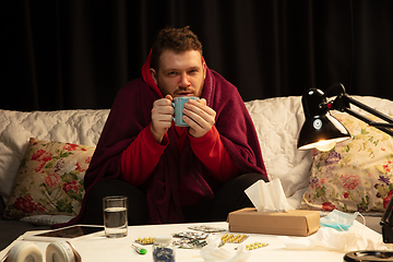 Image showing Man wrapped in a plaid looks sick, ill, sneezing and coughing sitting at home indoors