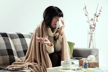 Image showing Woman wrapped in a plaid looks sick, ill, sneezing and coughing sitting at home indoors