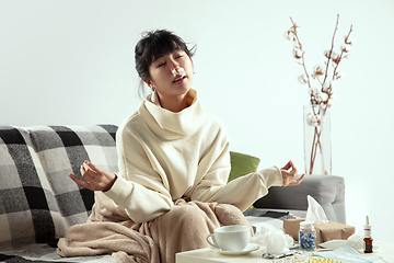 Image showing Woman wrapped in a plaid looks sick, ill, sneezing and coughing sitting at home indoors