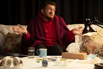 Image showing Man wrapped in a plaid looks sick, ill, sneezing and coughing sitting at home indoors