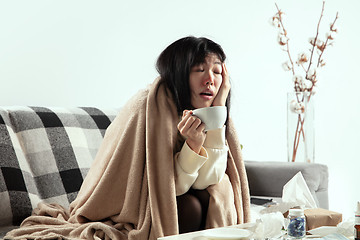 Image showing Woman wrapped in a plaid looks sick, ill, sneezing and coughing sitting at home indoors