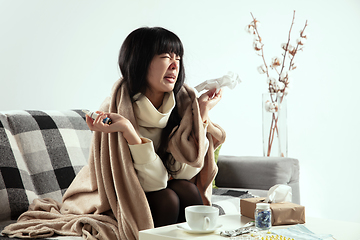 Image showing Woman wrapped in a plaid looks sick, ill, sneezing and coughing sitting at home indoors