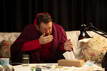 Image showing Man wrapped in a plaid looks sick, ill, sneezing and coughing sitting at home indoors