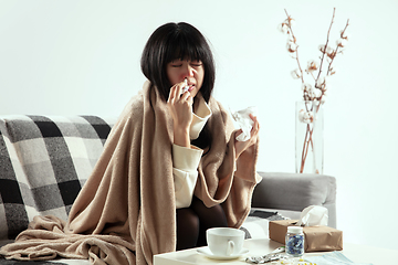 Image showing Woman wrapped in a plaid looks sick, ill, sneezing and coughing sitting at home indoors