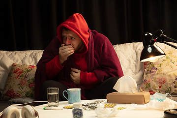 Image showing Man wrapped in a plaid looks sick, ill, sneezing and coughing sitting at home indoors