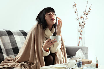 Image showing Woman wrapped in a plaid looks sick, ill, sneezing and coughing sitting at home indoors