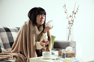 Image showing Woman wrapped in a plaid looks sick, ill, sneezing and coughing sitting at home indoors