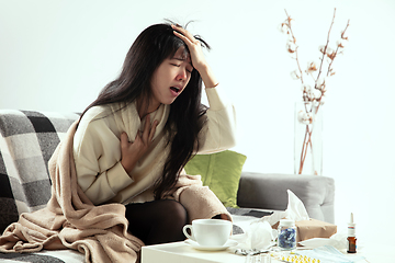 Image showing Woman wrapped in a plaid looks sick, ill, sneezing and coughing sitting at home indoors