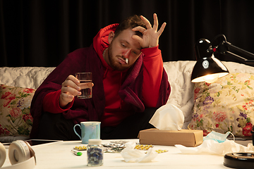 Image showing Man wrapped in a plaid looks sick, ill, sneezing and coughing sitting at home indoors