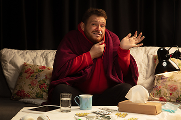 Image showing Man wrapped in a plaid looks sick, ill, sneezing and coughing sitting at home indoors