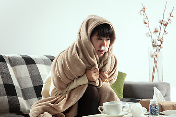 Image showing Woman wrapped in a plaid looks sick, ill, sneezing and coughing sitting at home indoors