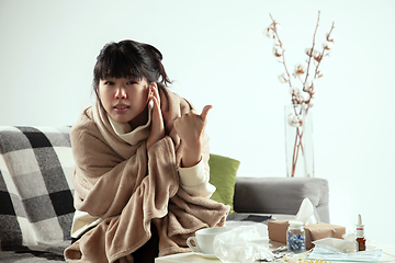 Image showing Woman wrapped in a plaid looks sick, ill, sneezing and coughing sitting at home indoors