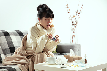 Image showing Woman wrapped in a plaid looks sick, ill, sneezing and coughing sitting at home indoors