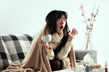 Image showing Woman wrapped in a plaid looks sick, ill, sneezing and coughing sitting at home indoors