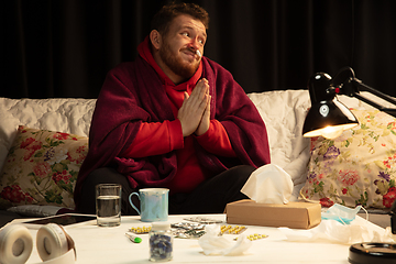 Image showing Man wrapped in a plaid looks sick, ill, sneezing and coughing sitting at home indoors