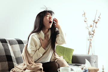 Image showing Woman wrapped in a plaid looks sick, ill, sneezing and coughing sitting at home indoors