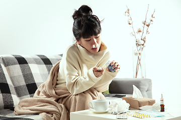 Image showing Woman wrapped in a plaid looks sick, ill, sneezing and coughing sitting at home indoors